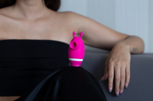 persona femenina reposando en un sillón en ropa negra con una pierna arrodillada y encima de ella un juguete sexual de color rosa con blanco.